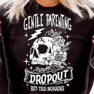 May include: Black and white graphic design featuring a skull with flowers and a banner that reads "Gentle Parenting Dropout Est: This Morning".