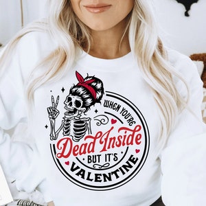 May include: White sweatshirt with a black and red graphic design featuring a skeleton with a peace sign and the text "When you're Dead Inside But It's Valentine".