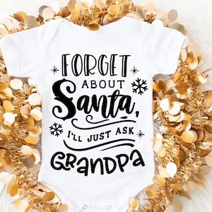 以下が含まれることがあります： 白いベビーロンパースに、黒い文字で「*FORGET* ABOUT Santa, *I'LL JUST ASK* Grandpa」と書かれています。ロンパースは金色のモールで囲まれています。