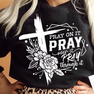 May include: A black sweatshirt with a white cross, flowers, and the text "Pray on it Pray over it Pray through it".
