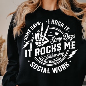May include: Black sweatshirt with a white graphic design that says "Some days I rock it. Some days it rocks me. Either way, we're rockin' social work."