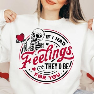 Puede incluir: Sudadera blanca con un gráfico negro y rojo de un esqueleto sosteniendo un corazón. El gráfico dice "Si tuviera sentimientos, serían para ti."