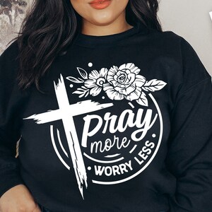 May include: A black sweatshirt with a white graphic design featuring a cross, a rose, and the text "Pray More Worry Less".