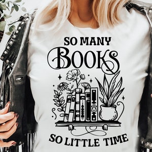 May include: A white t-shirt with a black graphic design that reads "SO MANY BOOKS SO LITTLE TIME". The graphic features a stack of books with flowers and a potted plant.