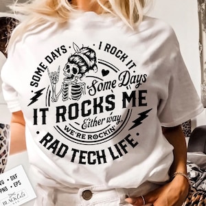 May include: White t-shirt with a black and white graphic design featuring a skeleton with a heart and the text "Some days I rock it, Some days it rocks me, Either way, we're rockin', Rad Tech Life."