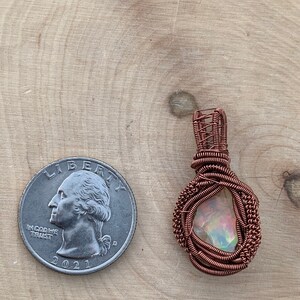 May include: A copper wire wrapped pendant featuring a iridescent gemstone. The pendant is approximately the size of a US quarter.