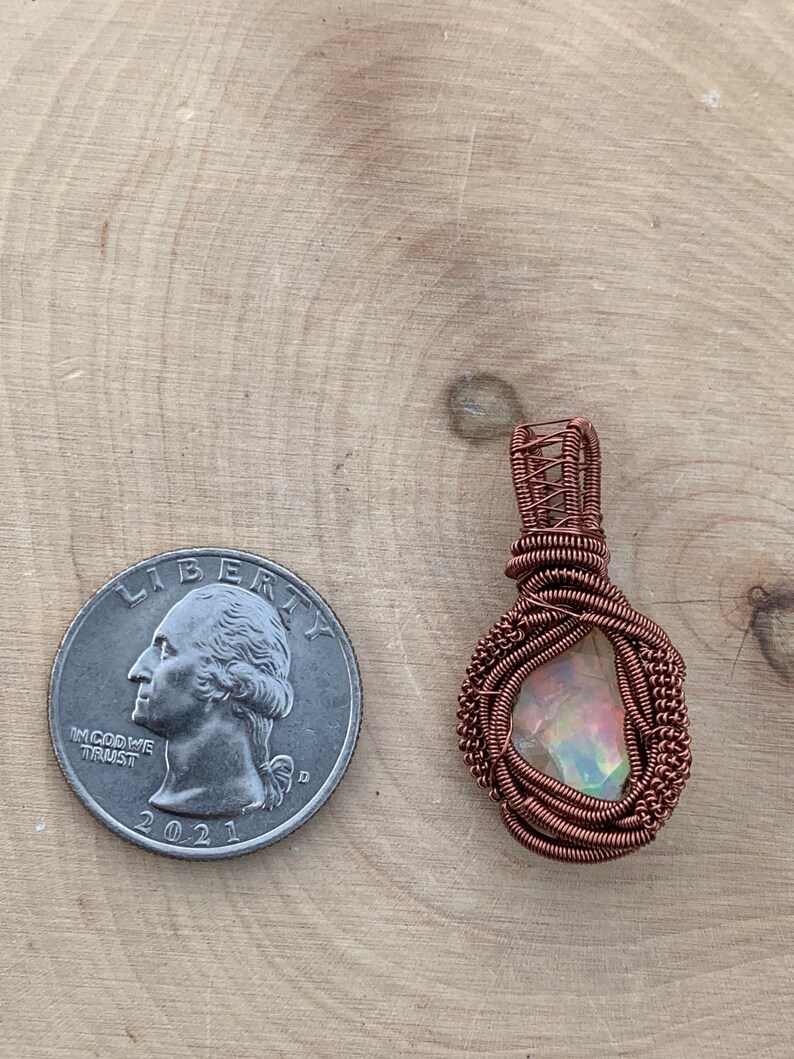 May include: A copper wire wrapped pendant featuring a iridescent gemstone. The pendant is approximately the size of a US quarter.