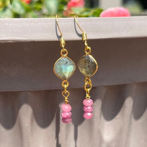 May include: Gold dangle earrings with a green and gray gemstone and three pink gemstones.