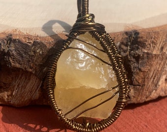 May include: A yellow crystal pendant wrapped in brass wire. The pendant is teardrop shaped and has a natural, rough texture.