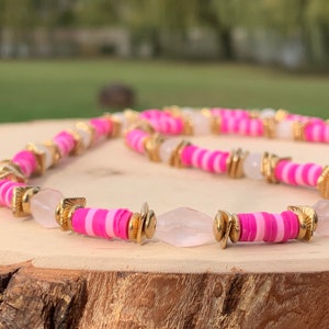 May include: A pink and white striped beaded necklace with gold accents and clear quartz beads.