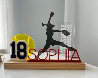 May include: A softball themed centrepiece with a yellow softball, a white number 18, and the name "Sophia" in red letters. The background features a silhouette of a softball player with the text "Riversville Diamonds".