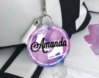 May include: A white and purple watercolor-style round keychain with the text "2020 Hershey Figure Skating" around the edge. The center of the keychain features a silhouette of a figure skater and the name "Amanda" in black script.