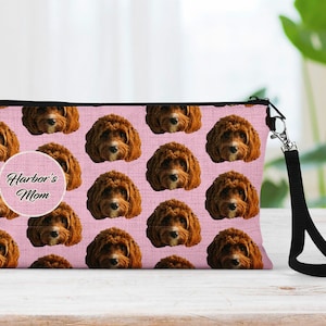 May include: Pink zippered makeup bag with a black strap. The bag is covered in a repeating pattern of brown dogs with the text "Harbor's Mom" in a white circle.