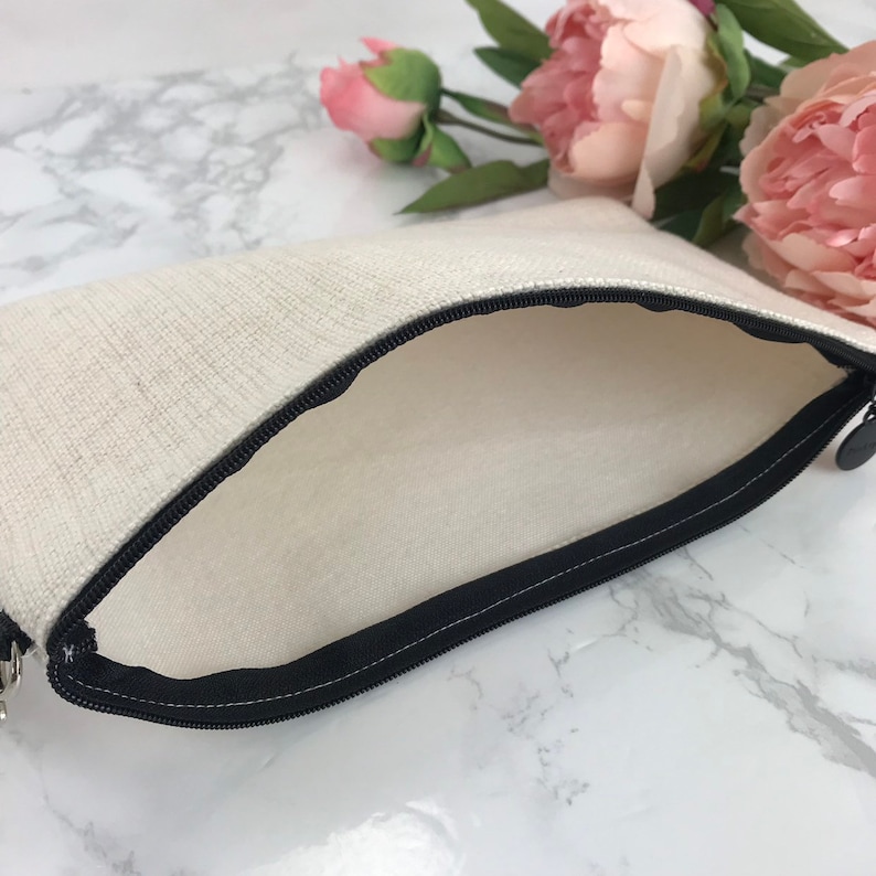 May include: A white canvas zippered pouch with a black zipper. The pouch is open and the inside is visible.