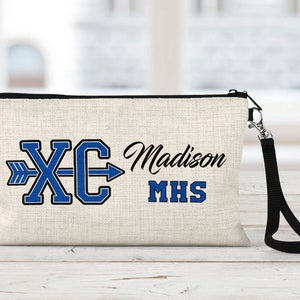 May include: A beige canvas zippered pouch with a black zipper and a black strap. The pouch has a blue and black embroidered design with the letters "XC" and an arrow pointing to the right. The text "Madison MHS" is also embroidered on the pouch.