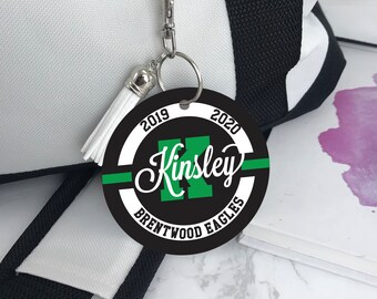 May include: Black and white round keychain with a green letter K, the name Kinsley, and the text "Brentwood Eagles 2019-2020".