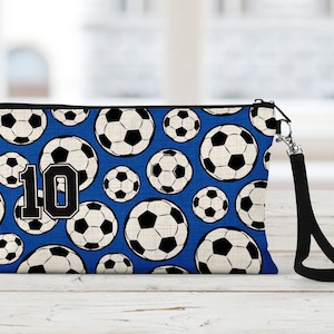 May include: A blue zippered pouch with a black strap. The pouch is covered in a pattern of white soccer balls on a blue background. The number "10" is printed in black on the front of the pouch.