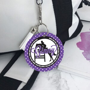 May include: Purple round keychain with white polka dots and the name "Ginny" in a black cursive font. A silhouette of a rider on a horse jumping over a hurdle is in the center of the keychain.