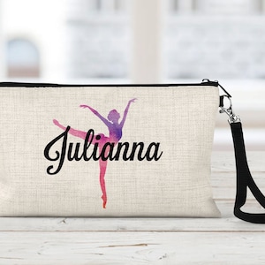 May include: A beige canvas makeup bag with a black zipper and a black strap. The bag features a watercolor-style silhouette of a ballerina with the name "Julianna" printed in black cursive.