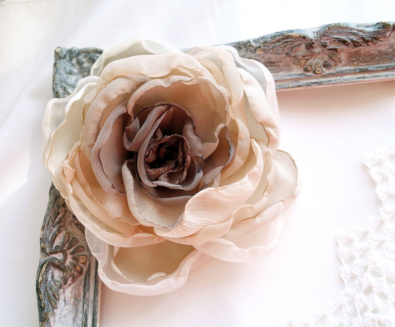 May include: A large, beige fabric flower with brown accents. The flower is made of multiple layers of fabric and has a delicate, ruffled appearance.