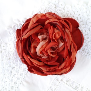 May include: A large, red fabric rose with a ruffled texture. The rose is made of layers of fabric that are gathered together to create a full, round shape.