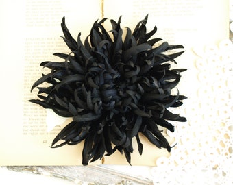 以下が含まれることがあります： 重ねてフリル状になった、大きな黒い布の花。花は、ドラマチックな効果を生み出すために、カールしてねじれた多くの花びらでできています。