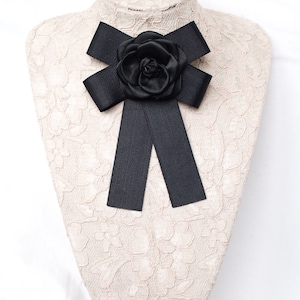 May include: A black satin bow with a large black flower accent. The bow is tied around a white lace-covered mannequin.