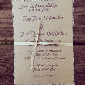 Puede incluir: Una invitaci&oacute;n de boda rectangular impresa en cartulina color canela con bordes de arpillera deshilachados, atada con una cinta fina de color crema. El texto dice: Love is friendship set on fire, Ray Jesse Schmuler & Jael Ragan McMillan.