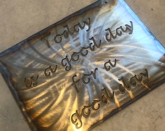 May include: A metal sign with a swirling pattern in shades of brown and gold. The sign reads "Today is a good day for a good day".