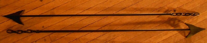 May include: Two black metal arrowheads with chains attached to the ends. The arrowheads are pointed and have a sharp edge. The chains are made of metal links.