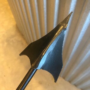 May include: A black metal arrowhead with a sharp point and a long, thin shaft.