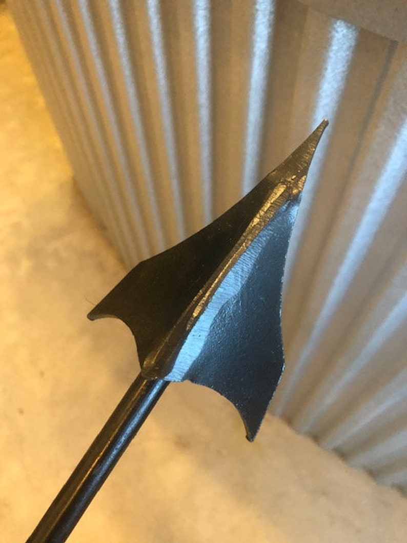 May include: A black metal arrowhead with a sharp point and a long, thin shaft.