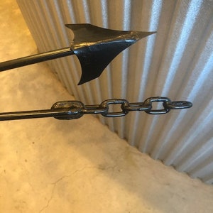 May include: A black metal anchor with a chain attached. The anchor has a sharp point and a flat base.