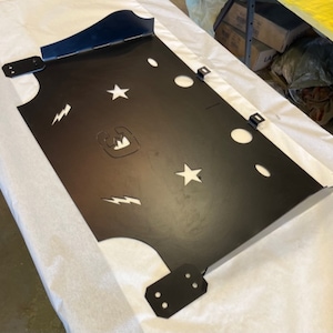 May include: Black metal plate with cutouts of stars, lightning bolts, and a logo. The plate has four mounting brackets.