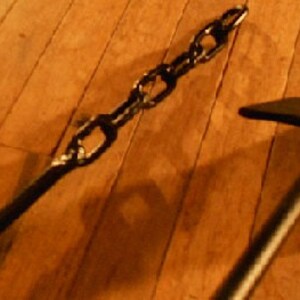 May include: A black metal chain and a black metal axe with a wooden handle. The axe and chain are lying on a wooden floor.