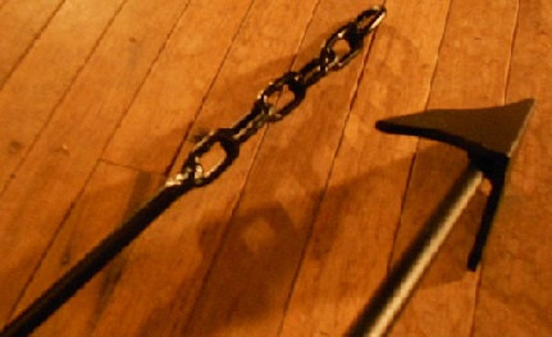 May include: A black metal chain and a black metal axe with a wooden handle. The axe and chain are lying on a wooden floor.