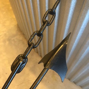 May include: A black metal spear with a chain attached to the top. The spear has a sharp point and a flat blade.