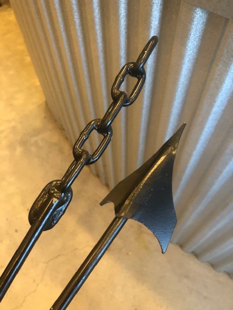 May include: A black metal spear with a chain attached to the top. The spear has a sharp point and a flat blade.