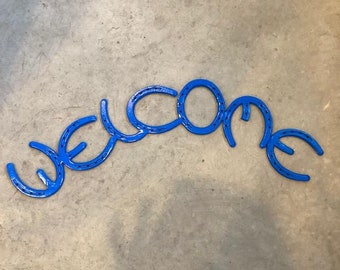 May include: A blue metal welcome sign made from horseshoes.