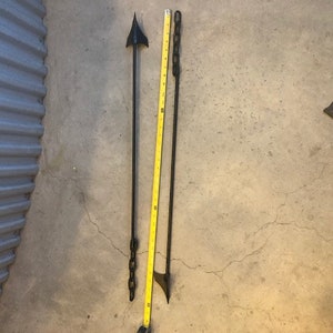May include: Two black metal rods with pointed ends. One rod has a chain attached to it. The rods are lying on a concrete floor.