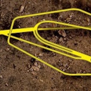 May include: A yellow metal rake with a long handle. The rake is lying on the ground.