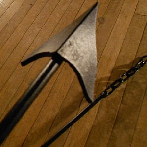 May include: A black metal weapon with a sharp point and a chain attached to the handle. The weapon is lying on a wooden floor.