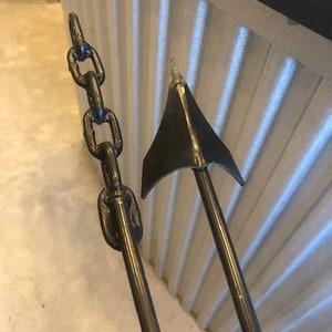 May include: A black metal anchor with a chain attached. The anchor is in the shape of a traditional ship anchor with a pointed tip and a curved arm.
