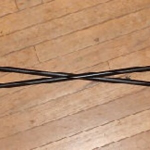 May include: Two black metal hooks with chain links attached, crossed over each other. The hooks are pointed and have a slight curve at the end.
