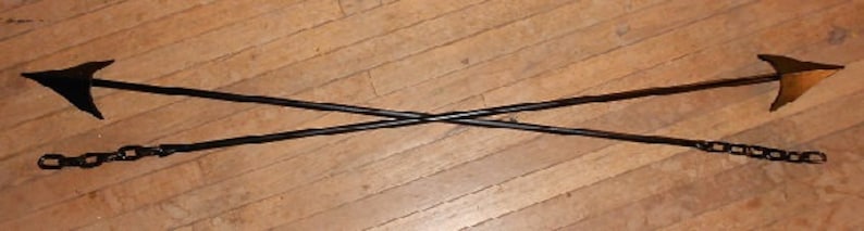 May include: Two black metal hooks with chain links attached, crossed over each other. The hooks are pointed and have a slight curve at the end.