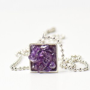 May include: A silver chain necklace with a square pendant featuring a cluster of purple amethyst crystals.
