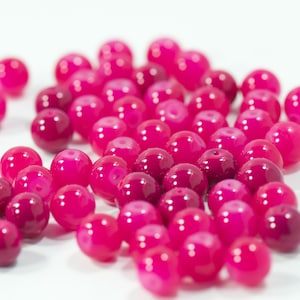 May include: A collection of vibrant, glossy, fuchsia-colored beads. These round beads vary in shade from deep magenta to bright pink, creating a visually appealing assortment. Ideal for jewelry making or craft projects.