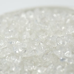 May include: A close-up of a pile of small, clear quartz crystals. The crystals are irregularly shaped and have a translucent appearance.