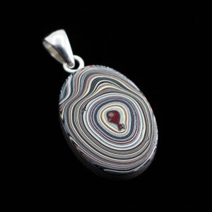 May include: A silver pendant featuring a colourful, oval-shaped agate stone with intricate concentric rings and a red centre.