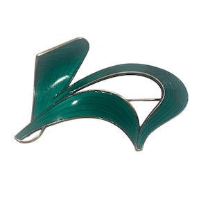 May include: A vintage brooch with a stylized leaf design. The brooch features a vibrant teal enamel finish with silver-toned metal edging. The design is abstract and elegant, suitable for adding a touch of color to any outfit.